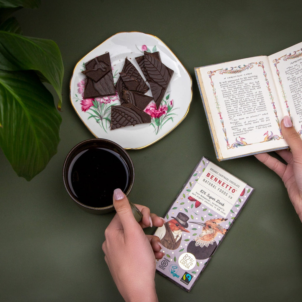 Chocolate bars on a plate with a cup of coffee, a book, and a box of Bennetto chocolate bars on a green surface.