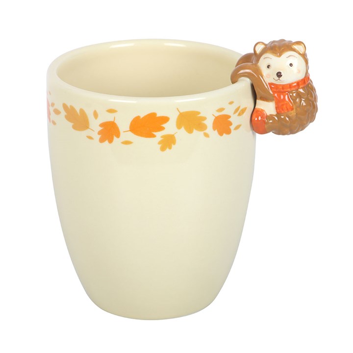 Cream-colored mug with a hedgehog handle and autumn leaf design on a white background