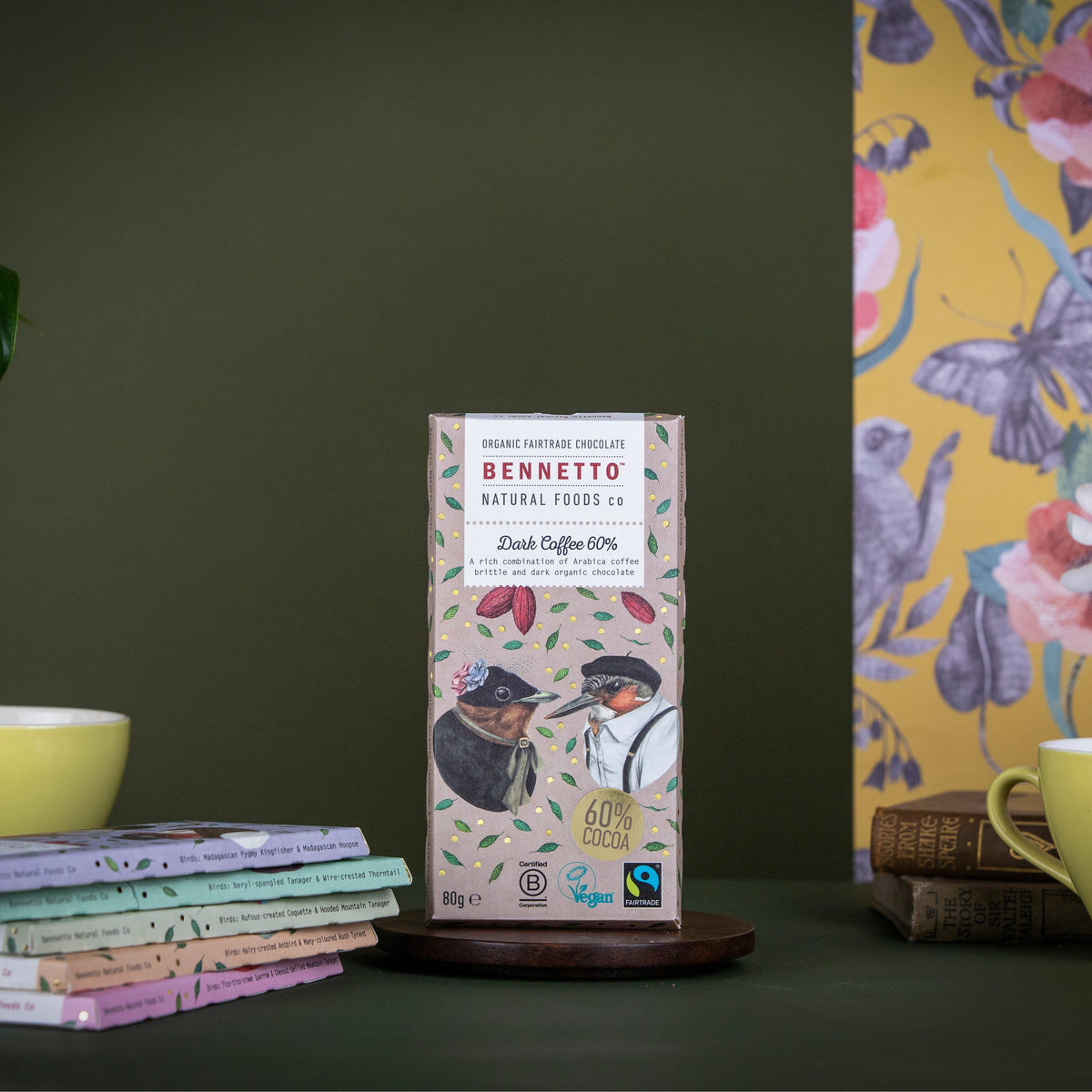 Bennetto natural foods co chocolate bar packaging on a dark surface with a colorful butterfly poster in the background.