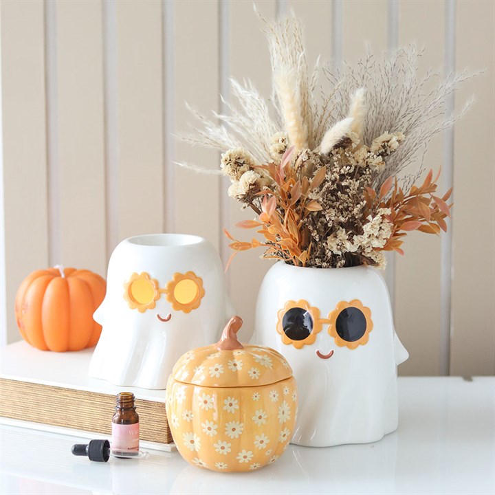 Decorative items including a pumpkin-shaped container, ghost-shaped lamps, and a vase with dried flowers on a table.