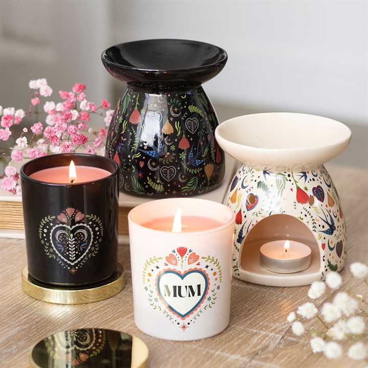 Decorative candles and oil burners with floral designs on a wooden surface.