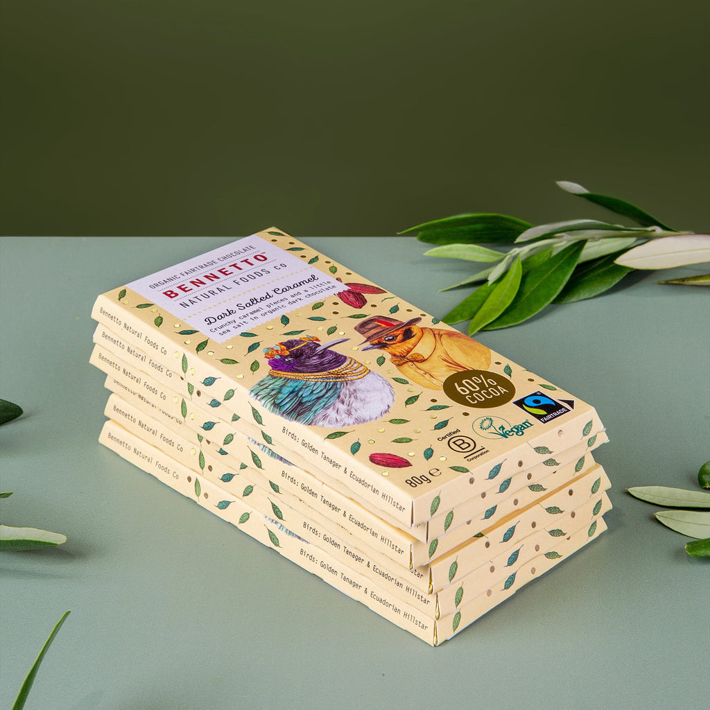 A stack of five chocolate bars in their packaging, styled with green leaves on a light sage green surface against a dark olive green background.