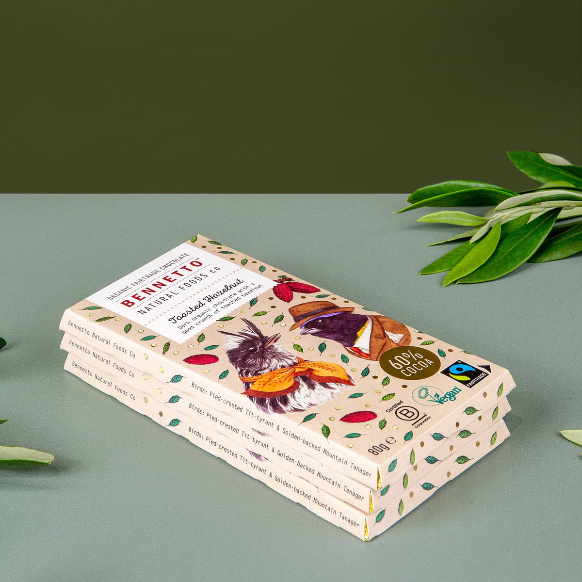 A stack of Berruto chocolate bars in decorative packaging, styled on a muted green surface with olive leaves in the corners.