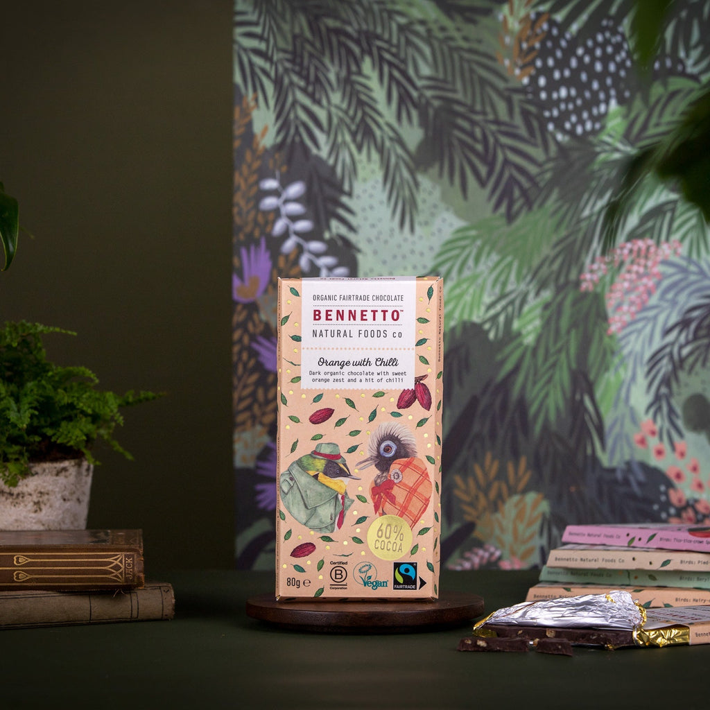 Bennetto natural food packaging on a dark surface with a colourful plant-patterned curtain in the background