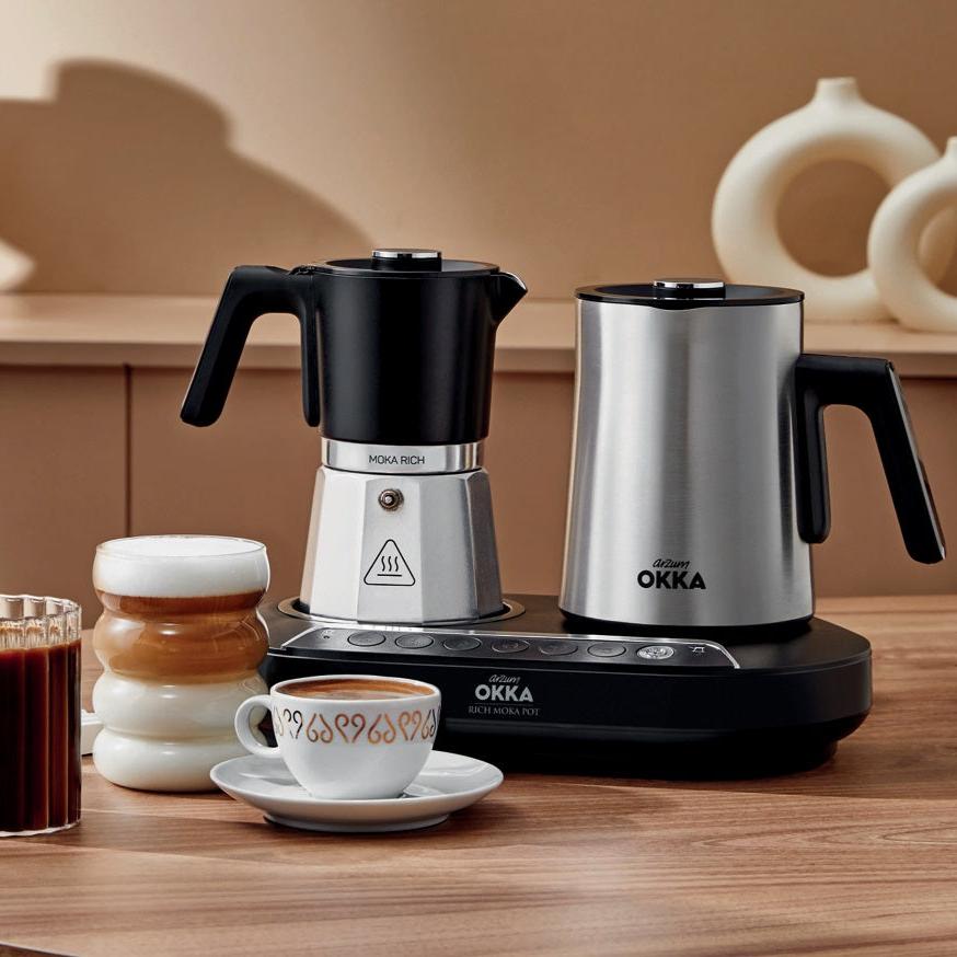 Two OKKA coffee makers on a wooden surface with a cup of coffee and a jar of cream.