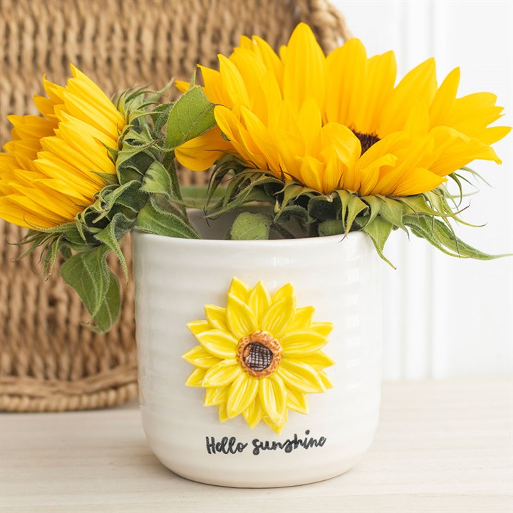 White plant pot with sunflower design and 'Hello Sunshine' text, filled with sunflowers.