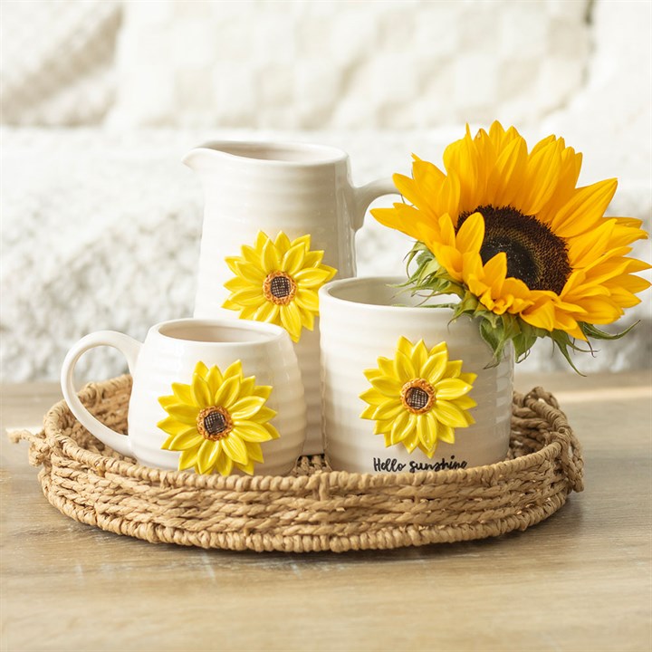 Three ceramic pots with sunflower designs on a woven tray, with sunflowers in the background.