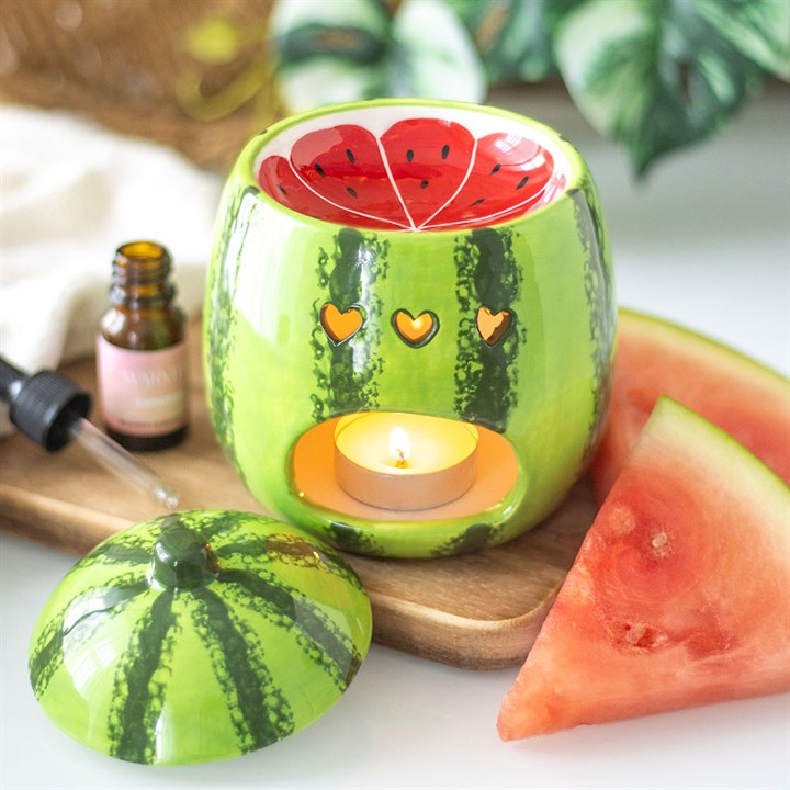 Watermelon-themed candle holder with a lit candle, surrounded by watermelon slices and essential oil bottle.