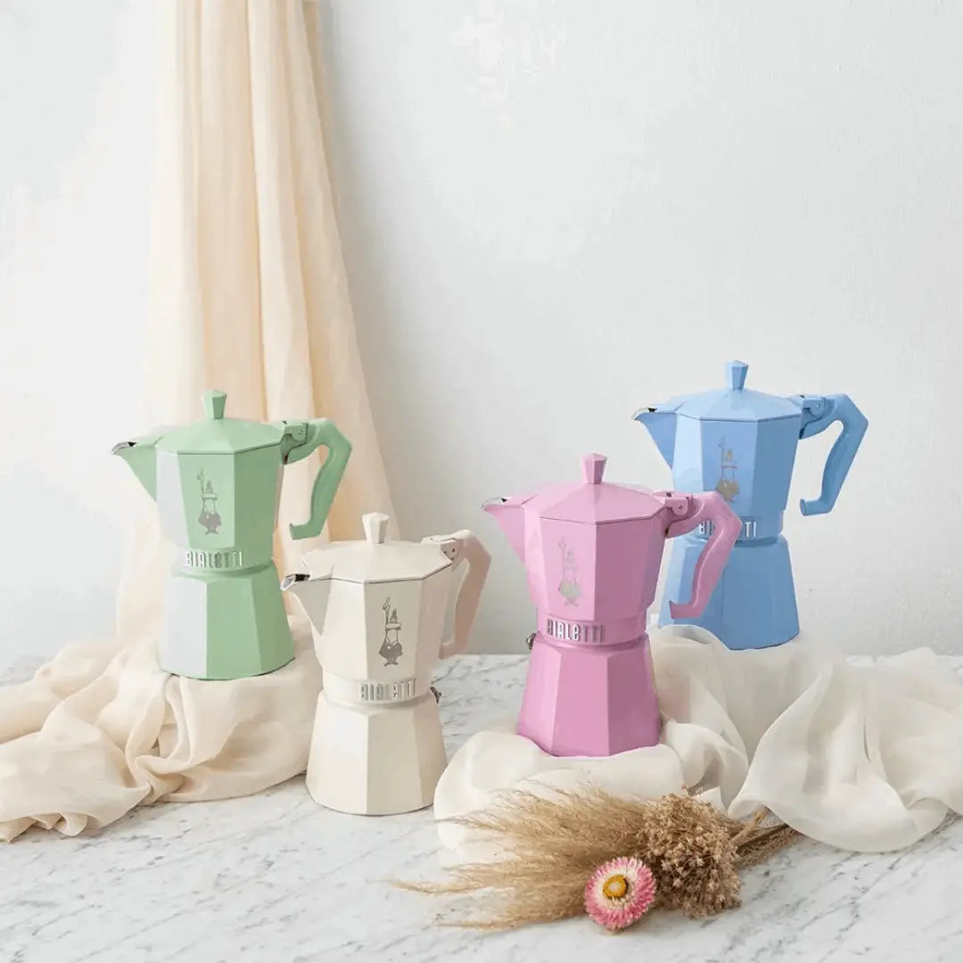 Four colourful coffee mokka kettles on a light surface with a neutral background